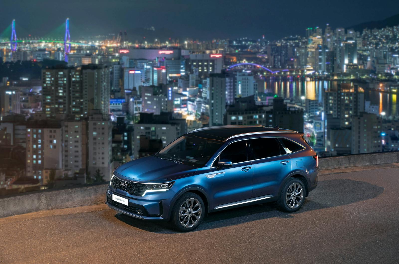 A Kia Sorento parked on a hill with the dazzling Busan skyline in the background during nighttime.